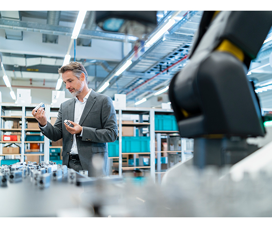 Engineer inspecting manufactured components beside automated production equipment in a modern factory